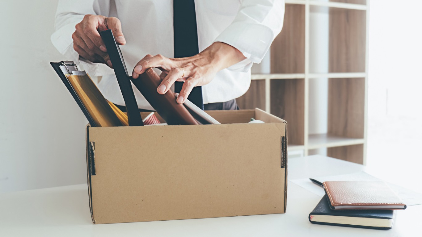 Eine Person packt persönliche Unterlagen und Rahmen in eine Umzugskiste im Büro.