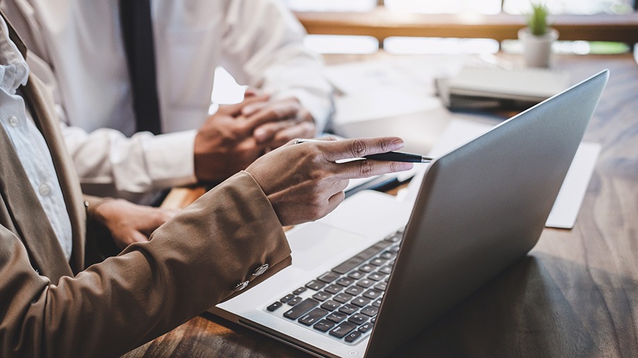 Zwei Personen besprechen etwas am Laptop, eine Hand zeigt mit einem Stift auf den Bildschirm.
